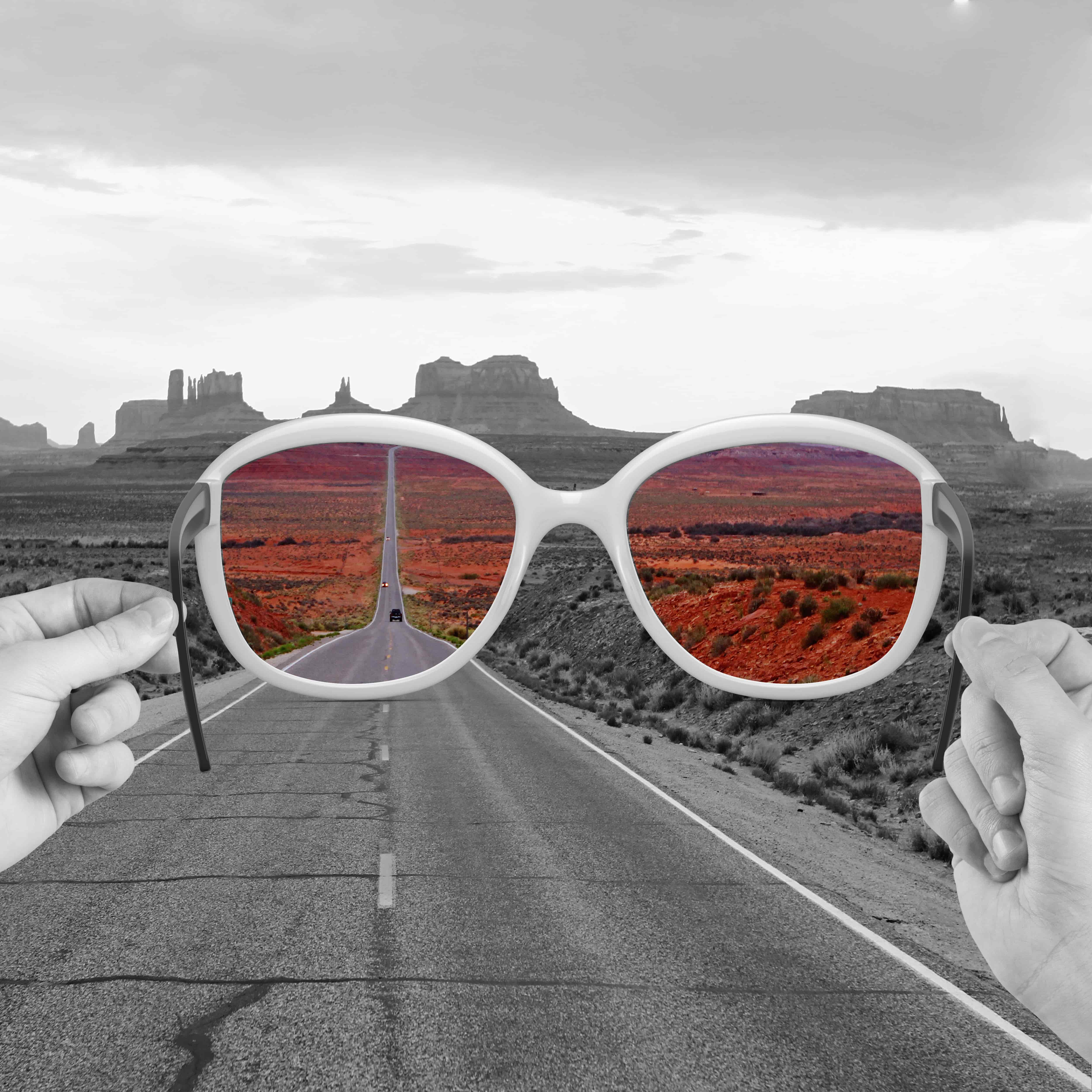 Varias manos mostrando gafas estenopeicas y opiniones impresas, con escaparate de óptica en Las Palmas al fondo.